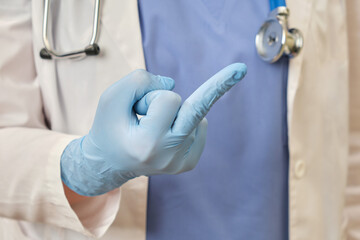 A hand in a medical glove shows the fuck you gesture. A doctor in a blue uniform makes an obscene...