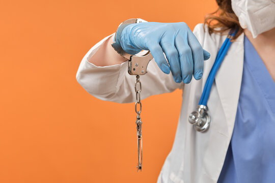 Doctor hands in handcuffs on red background, closeup. Woman hands in medical gloves handcuffed, coronavirus quarantine concept.