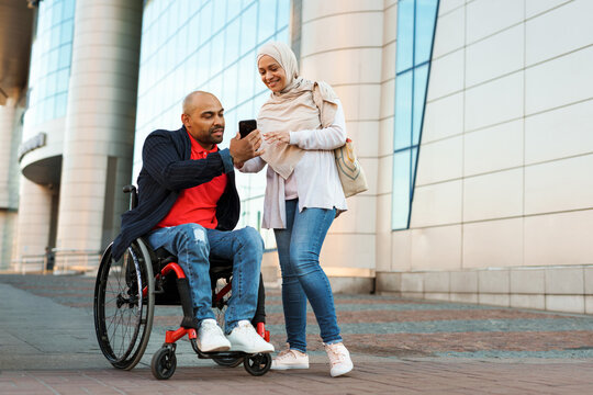 Muslim Woman And Man In Wheelchair Using Mobile Phone Together