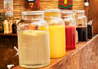 Bottle, jar of homemade lemon and orange lemonade. Three Large containers with a tap and various types of drinks stands on a bar counter at a picnic party, festival. Selective focus blurred background