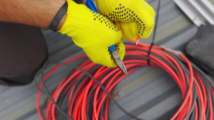 Electrician technician worker with wire stripper plier prepares the electric cable in electrical...