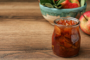 Tasty apple jam in glass jar and fresh fruits on wooden table, space for text