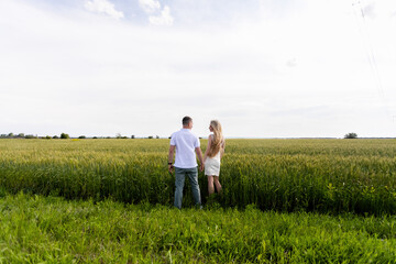 Naklejka na ściany i meble Young couple in the wheat field on sunny summer day. Couple in love have fun in golden field. Romantic couple in casual clothe outdoodrs on boundless field