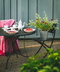 White tea set. Flowers in bucket. Table and chair outside.