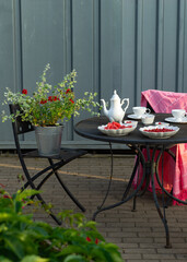 Summer outdoor setting. White tea set on table. Flowers in bucket.