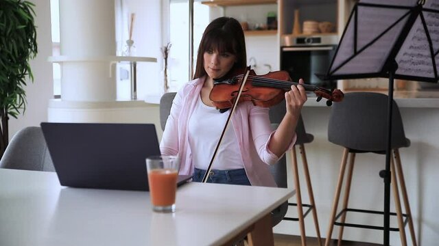 Young woman having online lesson of violin via laptop at home.