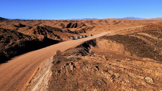 Srone shot of group of suv on desert serpentine road. Tourists having halt during expidition in african national park. Travellers exploring beauty of nature around cliffs and canyon shot by drone.