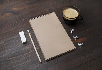 Photo of blank kraft notebook, pencil, eraser and coffee cup on wooden background. Template for branding identity.