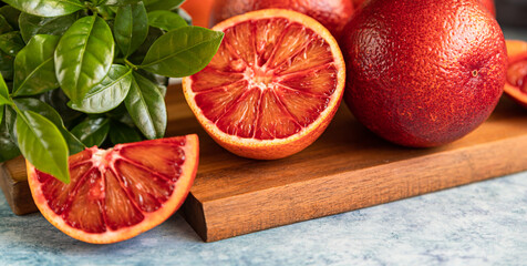 Sliced and whole ripe juicy Sicilian blood oranges on wooden cutting board with mint, blue concrete...