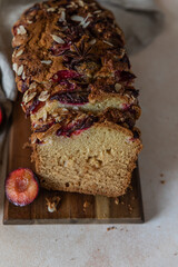 Homemade spicy plum cake decorated with almond on a wooden serving board, concrete background. Loaf cake with plum, spices and almond.