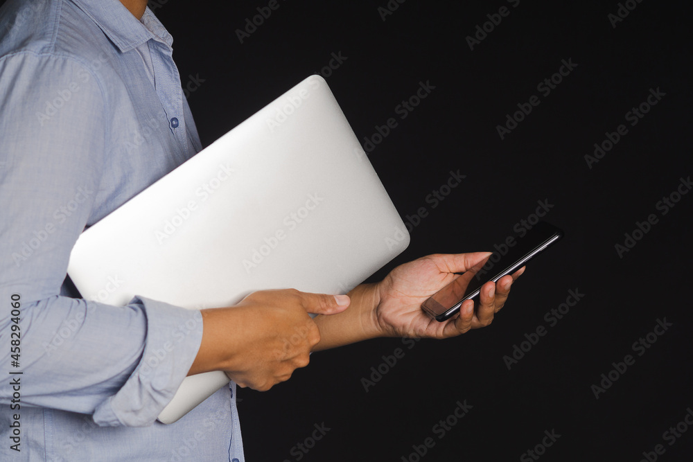 Poster businessman holding a laptop and using a smartphone while standing with black background in the stud