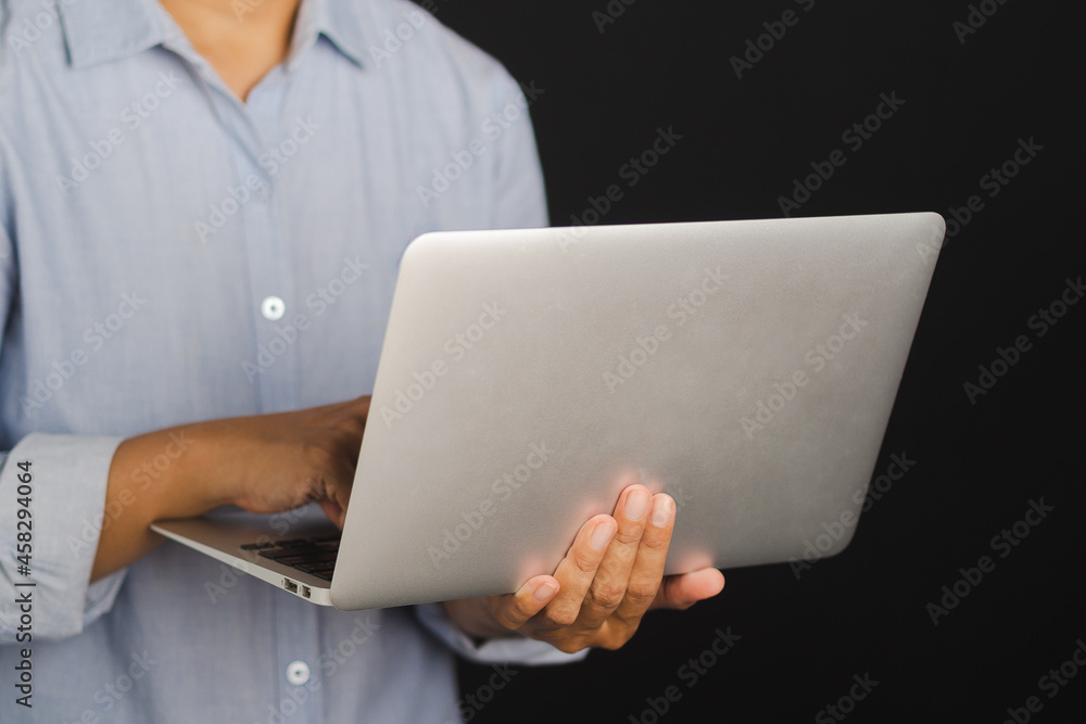 Poster businessman holding and using a laptop while standing with black background in the studio. space for