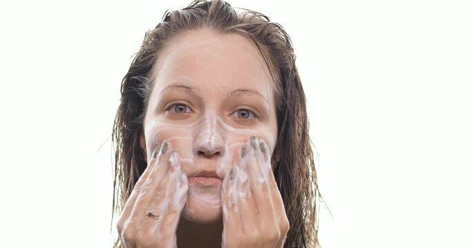 Portrait of young woman washing face with foamy gel. The girl with wet hair cleanses the skin after taking a shower, makes massage movements. Beauty treatments, spa, health and skin care concept.
