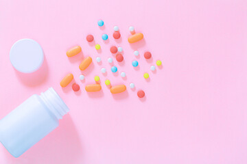 Multicolored tablets, pills, capsules in plastic bottle on pink background, copy space. Heap of assorted various medicine tablets and pills, vitamin and nutritional supplements concept.