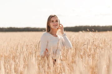 A young beautiful girl in a denim skirt walks through a wheat field on a sunny day