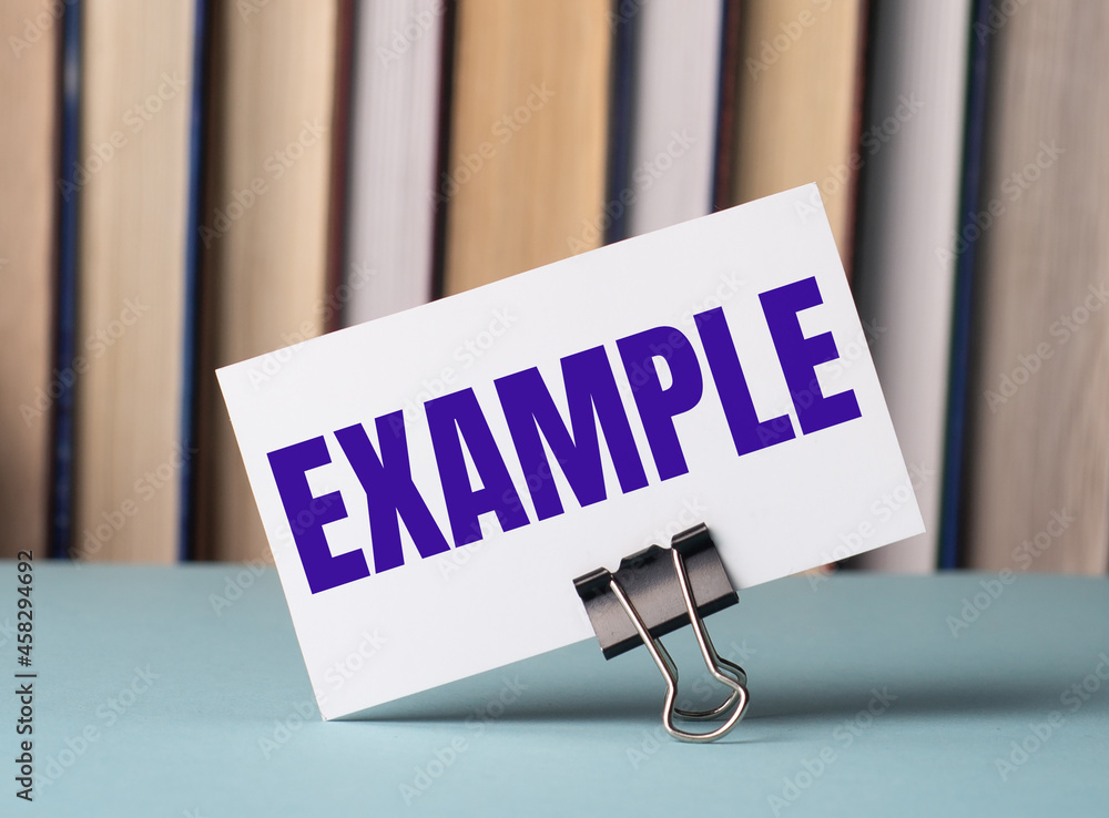 Aufkleber a white card with the text example stands on a clip for papers on the table against the background o