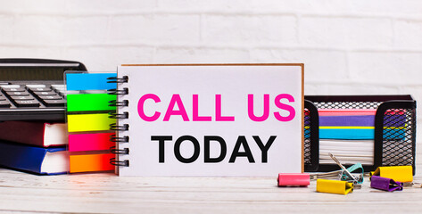 On a light wooden background, a calculator, multi-colored sticks and a notebook with the text CALL...