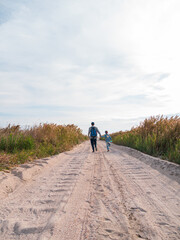Obraz premium Happy father and daughter running jumping having fun on empty autumn sea beach. Dad and child walking on white sand road with reeds blue sky background. Lifestyle real people. Happiness travel concept