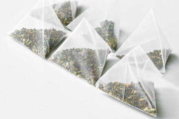 Six triangular tea bags-pyramids with green tea lie on a white background. Diagonal. Free space for an inscription