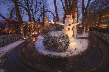 Decorative Christmas lights and winter decorations at Tivoli Gardens theme park and snowman around a toy train track in Copenhagen, Denmark.