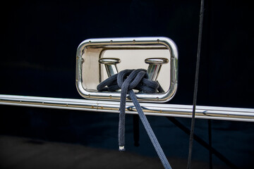 Stainless steel polished bollard with mooring rope on the dark blue hull of the super luxury yacht.