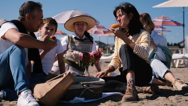 Happy family with children and older generation relaxing on the beach and eating vegetables and fruits having fun together during a picnic on the beach