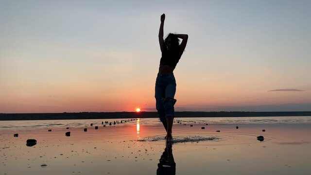 Silhouette of a beautiful woman dancing in the background of the sunset in the water. Ballet, dance, improvisation of contemporary dance.
