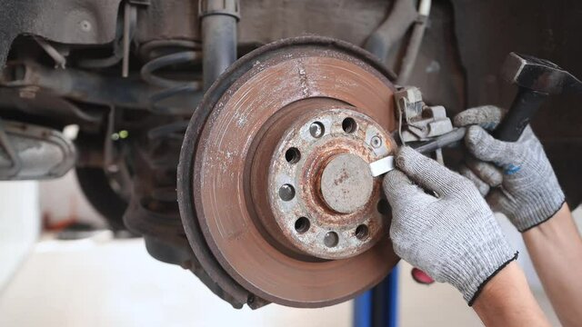 A mechanic uses a hammer and a chisel to unscrew the old brake disc on the wheel of a car for replacement, dismantling the vehicle.