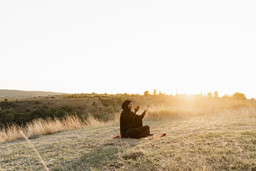 Black muslim woman praying to Allah at sunset. Solat traditional praying to god on the carpet.