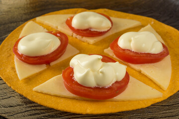 Sauce on slices of cherry tomatoes on slices of cheese on a tortilla