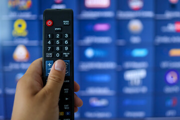 Smart tv and hand pressing remote control.Hand holding TV remote control with a television in the background. Close up.