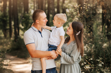Fototapeta premium Beautiful family parents and a young son in a wheat field. Mom, Dad and Baby Together. Happy family, parents hugs their little son
