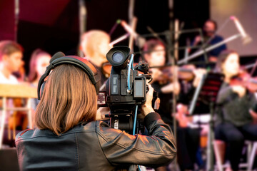A female videographer is filming the concert with a video camera.