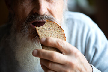An old man eats bread, face and mouth close up