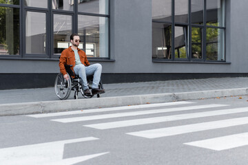 young handicapped man sitting in wheelchair near border and crosswalk - obrazy, fototapety, plakaty