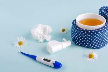 Cup of chamomile tea, thermometer, crumpled paper wipes and spray for runny nose and throat on blue background. Seasonal diseases and treatment of colds, flu, heat. Prevention of virus.