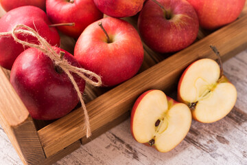 A lot of fresh red apples, one of them is tied with twine in a small wooden tray and two haves of an aplle next to the tray