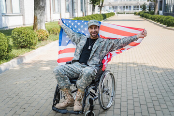 happy disabled veteran looking at camera while sitting in wheelchair with usa flag - obrazy, fototapety, plakaty
