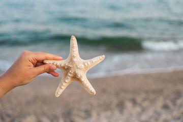 Fototapeta na wymiar Hand holding starfish with beautiful tropical summer sand beach island, relaxing vacation summer blue sea concept.