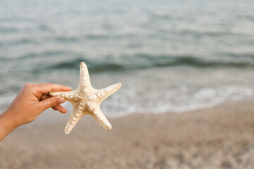 Hand holding starfish with beautiful tropical summer sand beach island, relaxing vacation summer blue sea concept.