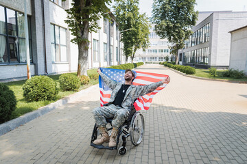 overjoyed handicapped military man in wheelchair holding usa flag and laughing on city street