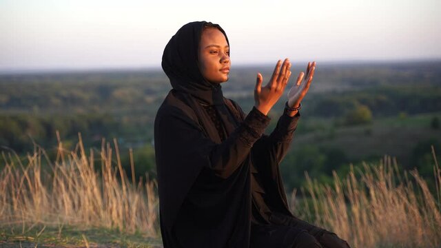 4k Black muslim woman praying on the carpet. Solat praying on the beautiful hill. Salah traditional pray.