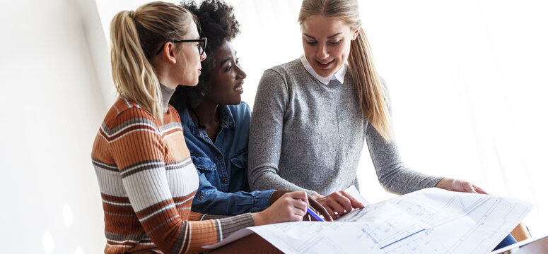 Group of design students sitting in classroom and examining blueprint.	
