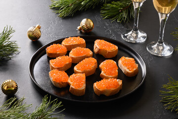 Festive Christmas canape with red caviar on ciabatta on a black background. Holidays party. Close up.