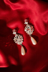 Women's earrings on red silk background. Elegant woman jewelry, close-up.