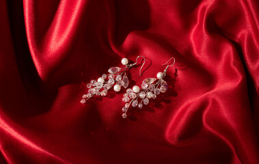 Women's earrings on red silk background. Elegant woman jewelry, close-up.