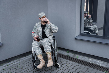 young disabled soldier in wheelchair drinking alcohol in corner of grey wall outdoors