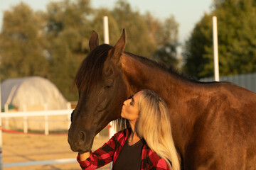 Young woman farmer in a red checkered shirt hugs her horse concept of love between people and animals.