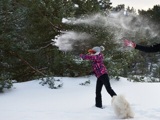 Zimowa bitwa na śnieżki. Rozbawiony biały pies próbuje schwytać lecące śnieżne kule.