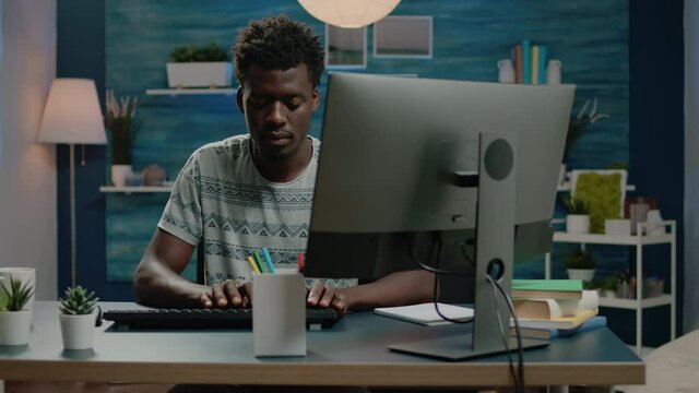 Adult of african ethnicity using computer for remote work and typing on keyboard. Businessman working from home with online technology and browsing internet. Person networking.